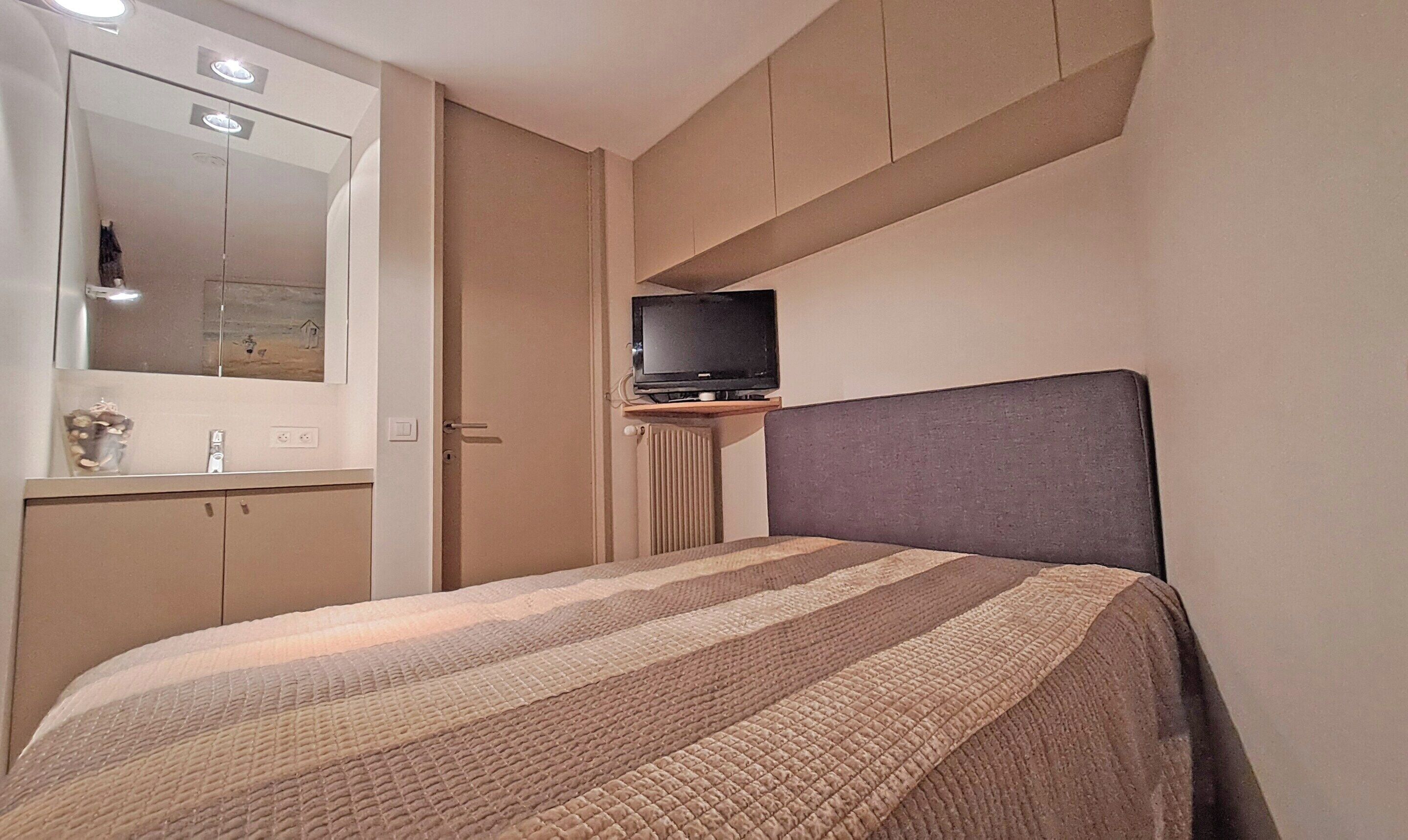 Un dormitorio con cama, televisor sobre un mueble, espejo y armario.