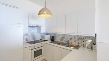 Una cocina moderna con gabinetes blancos, microondas, cafetera y lámpara colgante.