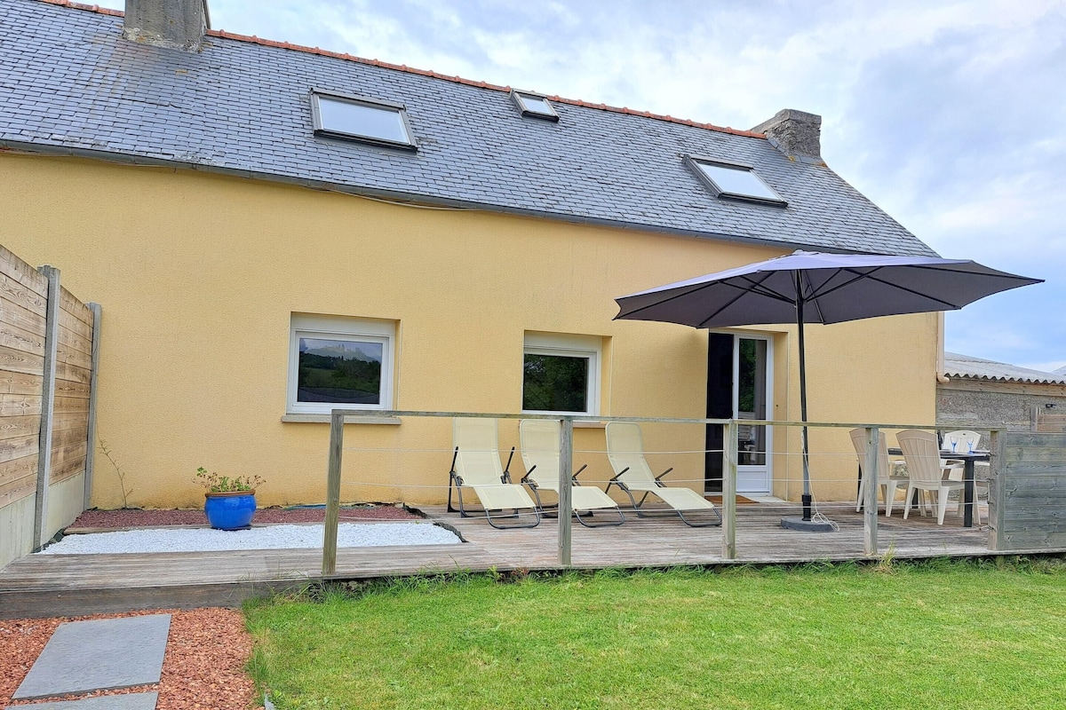 A yellow building with a tiled roof, a covered patio with lounge chairs, and a wooden fence.