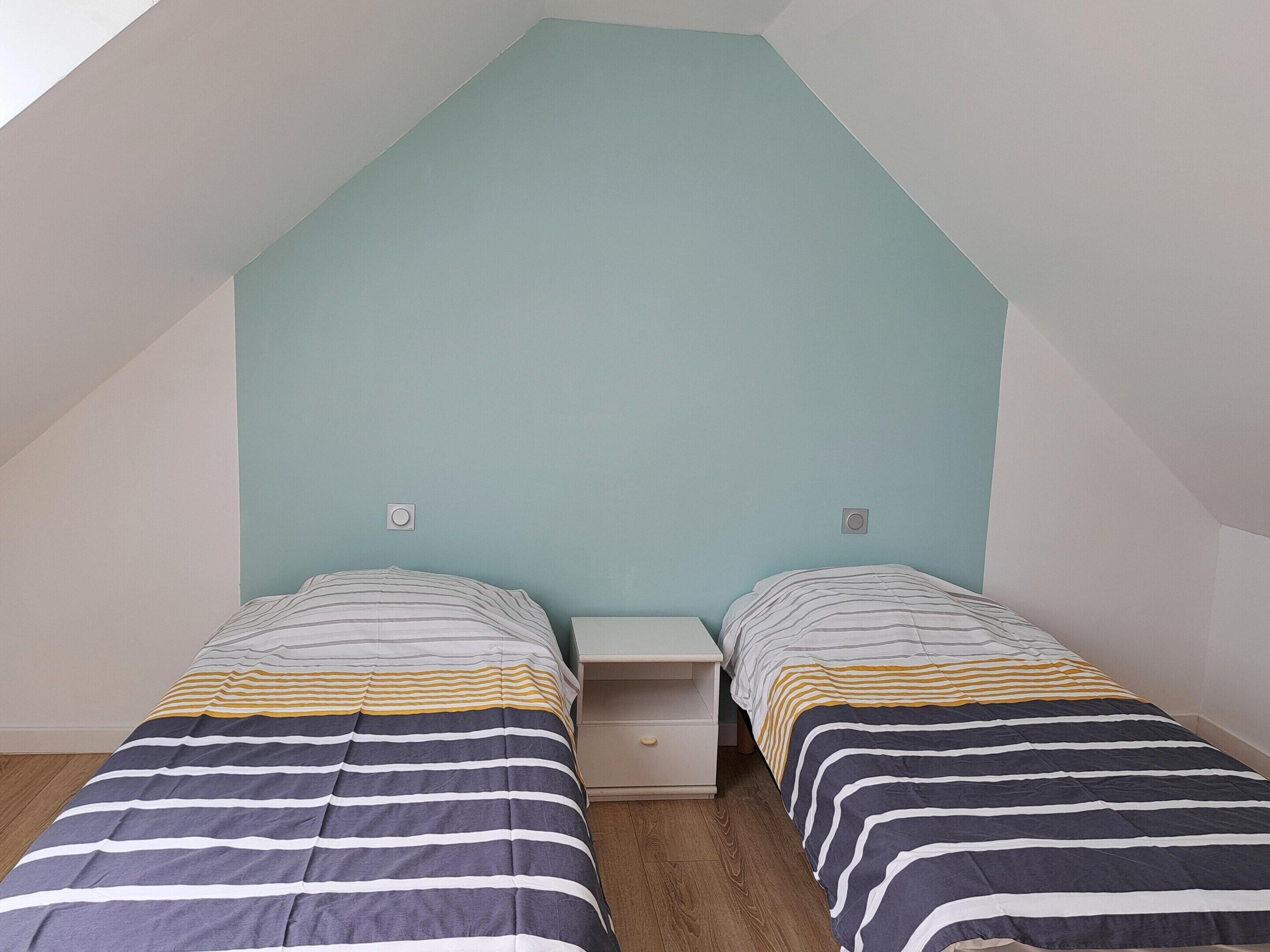 A small, simple room with two single beds, a nightstand, and a light blue accent wall.