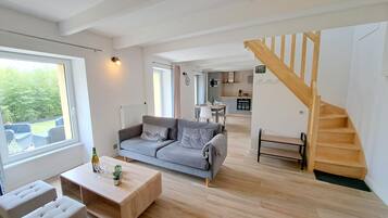 A spacious living area with a grey sofa, wooden coffee table, and a staircase leading to an upper level.