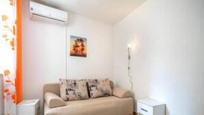A minimalist living room with a beige sofa, two side tables, an air conditioning unit, and a wall-mounted power outlet. - Studio in Vodice Near Male Vrulje Beach (Vodice)