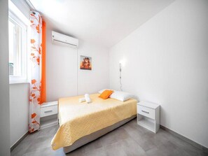 Ein Schlafzimmer mit Bett, Nachttisch, Wand-Klimaanlage und einem Fenster mit Vorhängen.