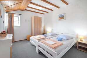 Une chambre avec deux lits, une armoire, un bureau, une fenêtre avec des rideaux et un tableau au mur.