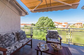 Un balcon avec un canapé, des chaises, une table avec des plateaux, et une vue sur les bâtiments et la verdure.