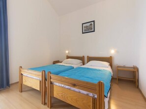 Una stanza con due letti di legno, un comodino, un quadro appeso al muro e una tenda.