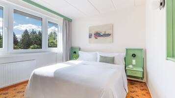 A hotel room with a large bed, a window with curtains, a green nightstand, and a painting on the wall.