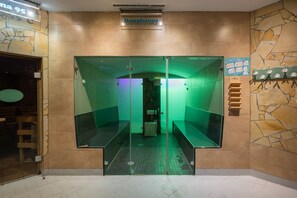 L'ingresso di una spa, con un cartello che riporta 'Dampfsana', una parete piastrellata con motivo in pietra e interni illuminati di verde.