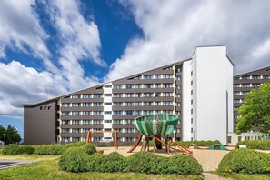 Ein modernes Hotel mit mehrstöckiger Struktur, einem Spielplatz mit Schaukeln und einem großen, grünen Sessel.