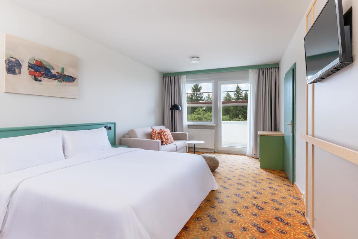 A hotel room with a bed, a sofa, a television, and a window with curtains.