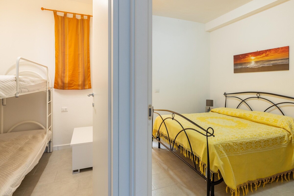 A bedroom with bunk beds, a single bed, a bedside table, a lamp, and a painting on the wall.