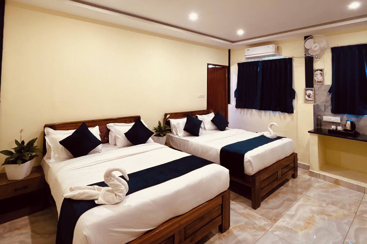 A hotel room with two wooden beds, a ceiling fan, a small table with a plant, and a bathroom with a mirror and curtains.
