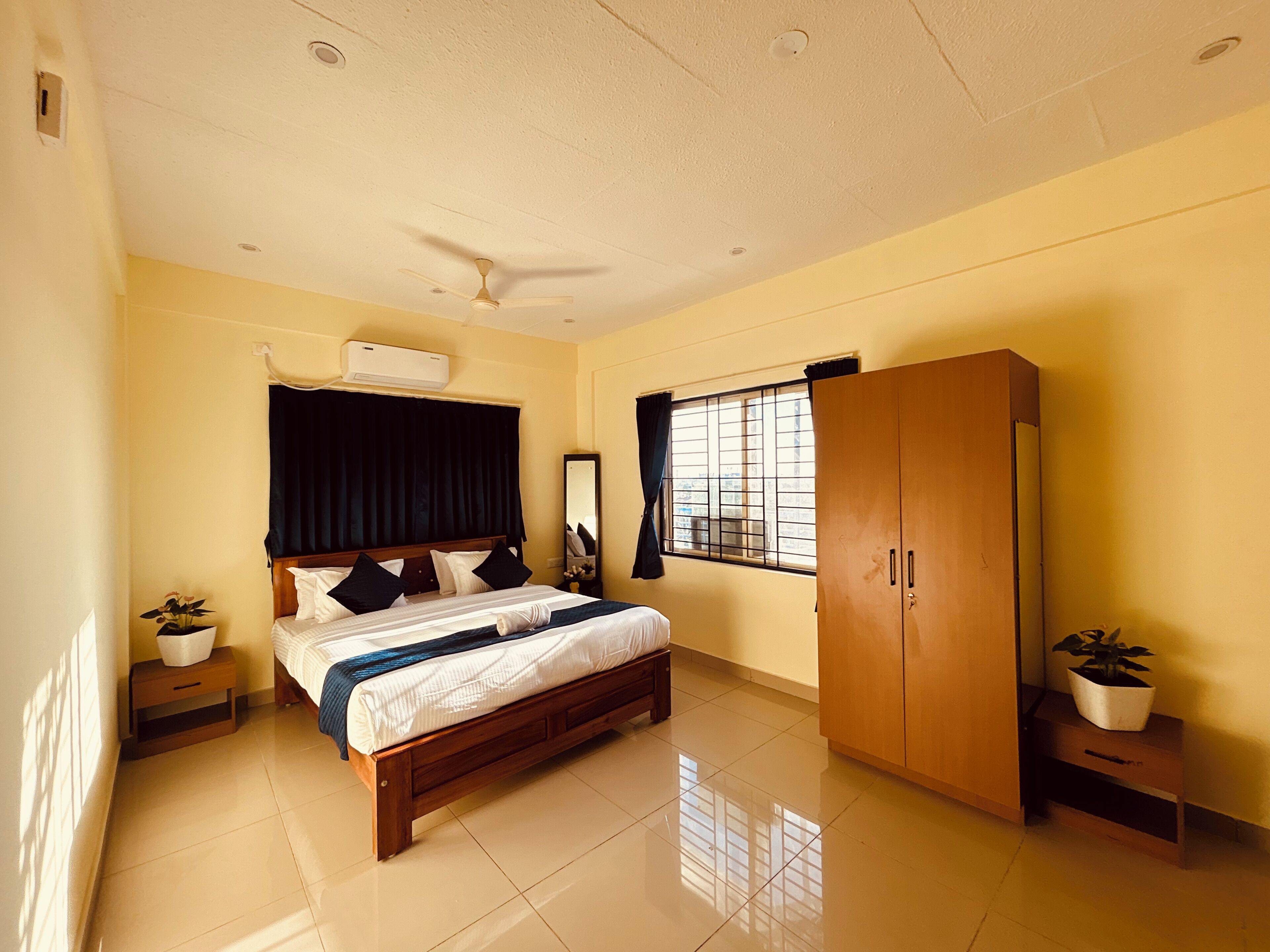 A bedroom with a bed, a wardrobe, a ceiling fan, a window with bars, and a potted plant.