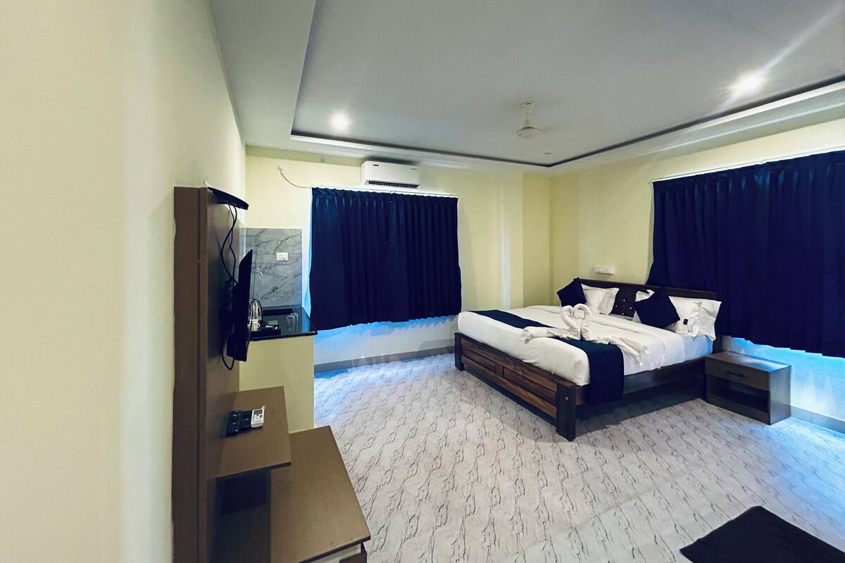 A modern hotel room with a large bed, bedside tables, a flat-screen TV, and a built-in air conditioning unit.