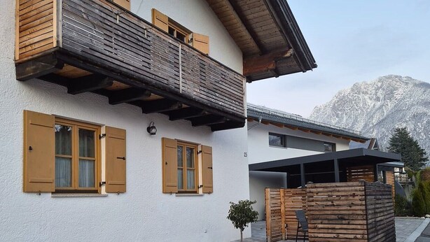 Un bâtiment à deux étages doté de balcons en bois, avec un petit arbre et une montagne en arrière-plan.