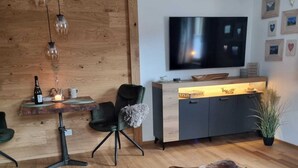Un salon moderne avec un mur en bois, un tapis en cuir, un téléviseur et un bureau agrémenté d’une plante.