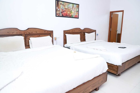 A hotel room with two wooden beds, white bedding, a painting on the wall, and a door. - Lake Alpi Resort Kumbhalgarh (Kumbhalgarh)