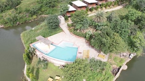 Vista aérea de um resort com piscina, cabanas de madeira e vegetação exuberante.