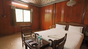 Um quarto de madeira com uma cama, duas cadeiras, uma mesa e uma janela. Há um controle remoto na mesa.