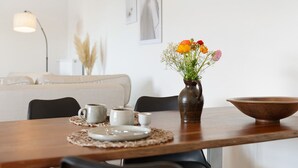 Ein Esstisch mit Blumen in einer Vase, einer Schüssel und einer Lampe in einem Raum mit einer Couch und Wandbildern.