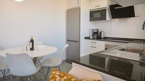 Uma cozinha moderna com geladeira, micro-ondas e pia. Há uma mesa de jantar com cadeiras e uma garrafa de vinho.