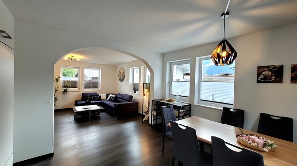 A modern living space with a dining area, a sofa set, and a dining table with chairs.