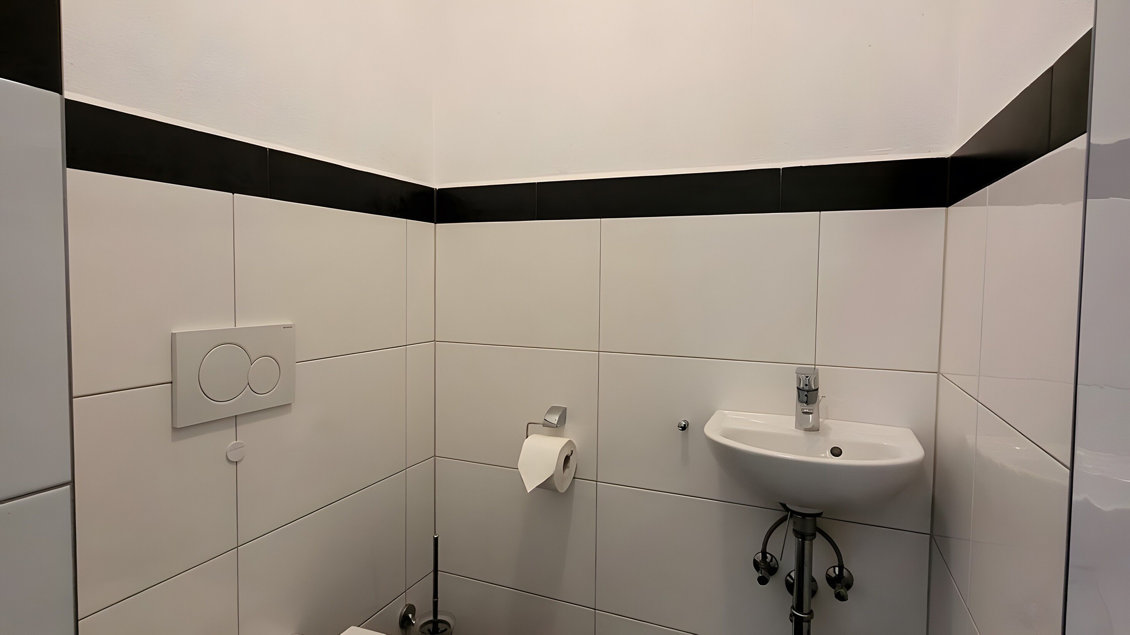 Un baño moderno con azulejos blancos, un lavamanos blanco y un inodoro.