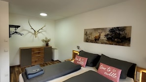 A bedroom with a bed, pillows, a dresser, a wall-mounted deer head, and a painting of deer.