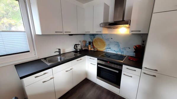 A modern kitchen with white cabinets, a black countertop, a stainless steel sink, a stove, and a microwave.