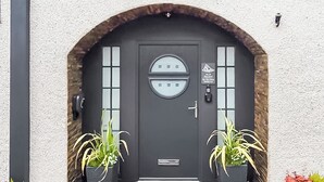 Una puerta gris oscura con un ventanal circular, dos plantas en macetas y una pequeña señal sobre la puerta.