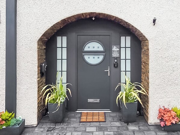Una puerta gris oscura con un ventanal circular, dos plantas en macetas y una pequeña señal sobre la puerta.