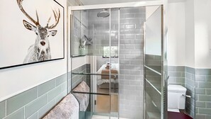 Un baño moderno con ducha acristalada, inodoro blanco y un cuadro de un ciervo enmarcado en la pared.