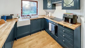 Una cocina moderna con armarios oscuros, encimera de madera, horno integrado y ventana con vista a árboles.