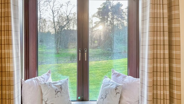 Una habitación con un ventanal grande, dos cojines blancos con estampado de ciervos y vistas a un patio cubierto de césped.