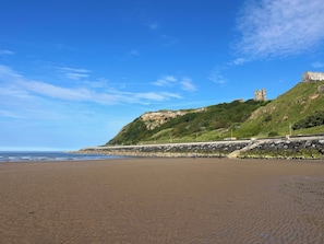 A beach with a stone wall, a grassy hill, and a castle ruin. - The Old School House (Scarborough)
