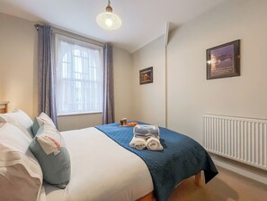 Ein Hotelzimmer mit einem Bett, einem fensterbelaubten Fenster, einem Heizkörper und zwei gerahmten Bildern an der Wand.