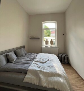 Een slaapkamer met een bed, een raam, een radiator en een vloerlamp.