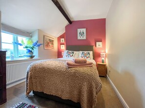 A bedroom with a bed, a nightstand, a lamp, a window with flowers, and wall art.