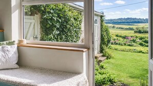 A cozy room with a built-in bench, a view of a garden, and a window overlooking greenery. - 1 bedroom accommodation in Weybourne (Weybourne)