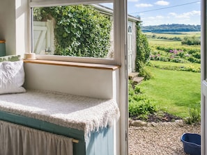 A cozy room with a built-in bench, a view of a garden, and a window overlooking greenery. - 1 bedroom accommodation in Weybourne (Weybourne)
