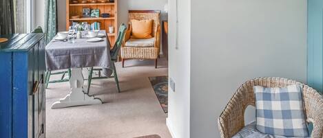 Ein Essbereich mit einem Tisch für vier Personen, einem Korbstuhl und einem Bücherregal mit diversen Gegenständen.