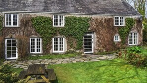 A stone house with ivy-covered walls, multiple windows, and a stone pathway leading to a wooden bench. - 4 bedroom accommodation in St. Teath (St. Teath)