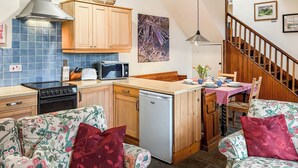 Cocina compacta con microondas, estufa y lavavajillas, armarios de madera y una zona de comedor con mesa y sillas.