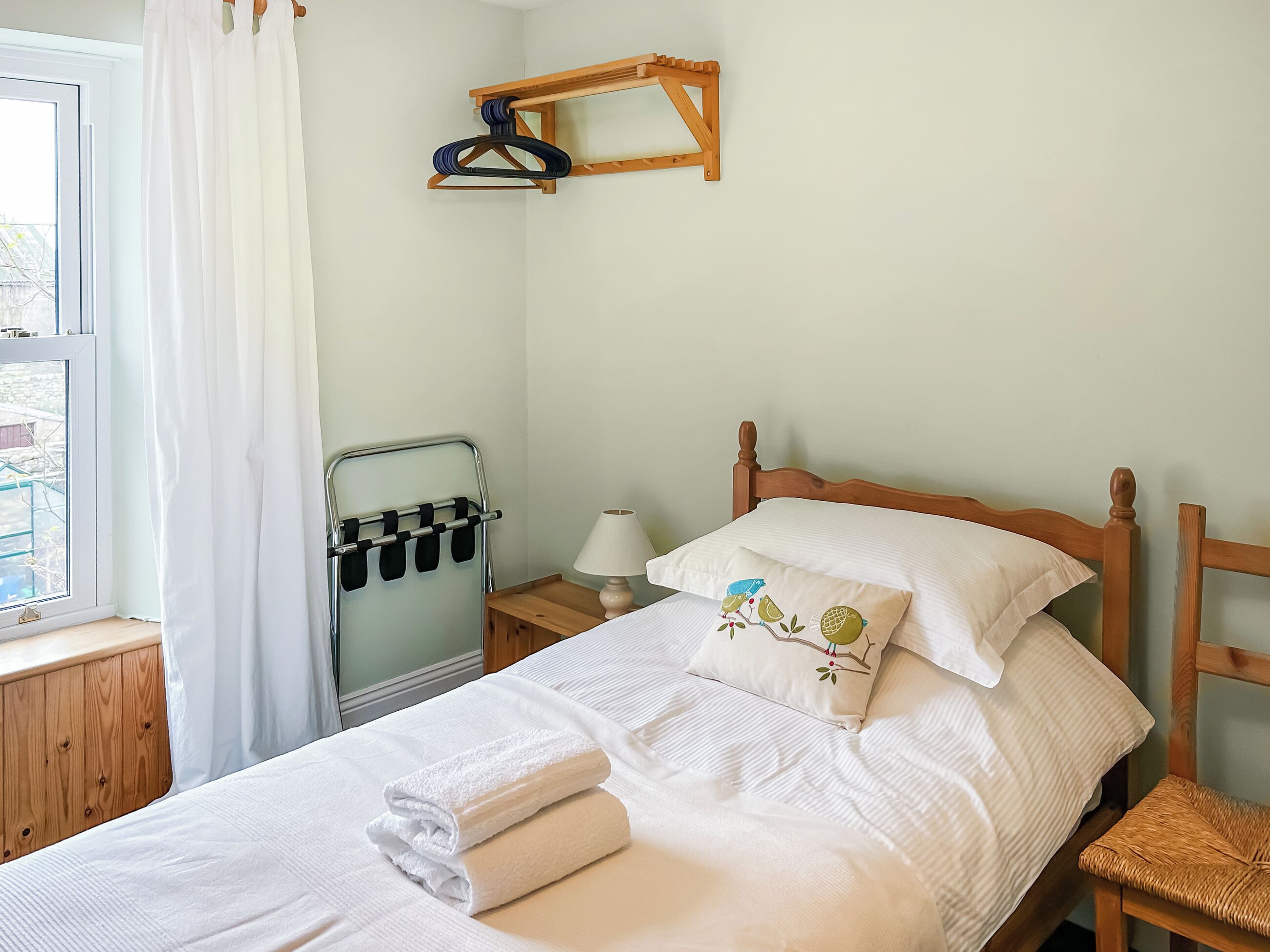 Un lit bien fait, avec du linge de lit blanc, une tête de lit en bois et une table de chevet surmontée d’une lampe.