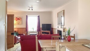Una sala de estar con un sofá rojo, una mesa de comedor de madera y una televisión.