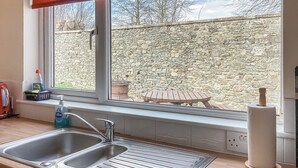 Una cocina con un lavamanos doble, una ventana que da a un muro de piedra y una mesa de madera afuera.