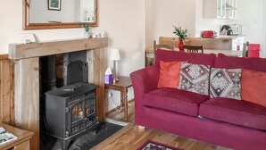 Una sala de estar con chimenea, un sofá rojo, una mesa de comedor de madera y una cocina al fondo.