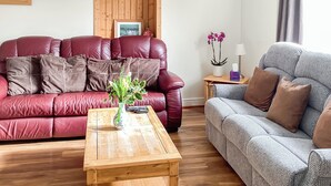 Ein Wohnzimmer mit einem roten Ledersofa, einem grauen Sofa, einem Holztisch und einem kleinen Beistelltisch mit Lampe und Blumen.