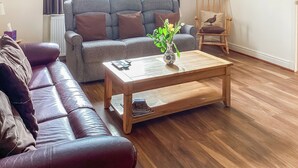 Ein Wohnzimmer mit einer Ledersofa, einem grauen Sofa, einem Couchtisch aus Holz mit einer Vase und einem Holzstuhl.