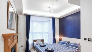 Un dormitorio con cama, escritorio, silla, chimenea y una ventana grande con cortinas.